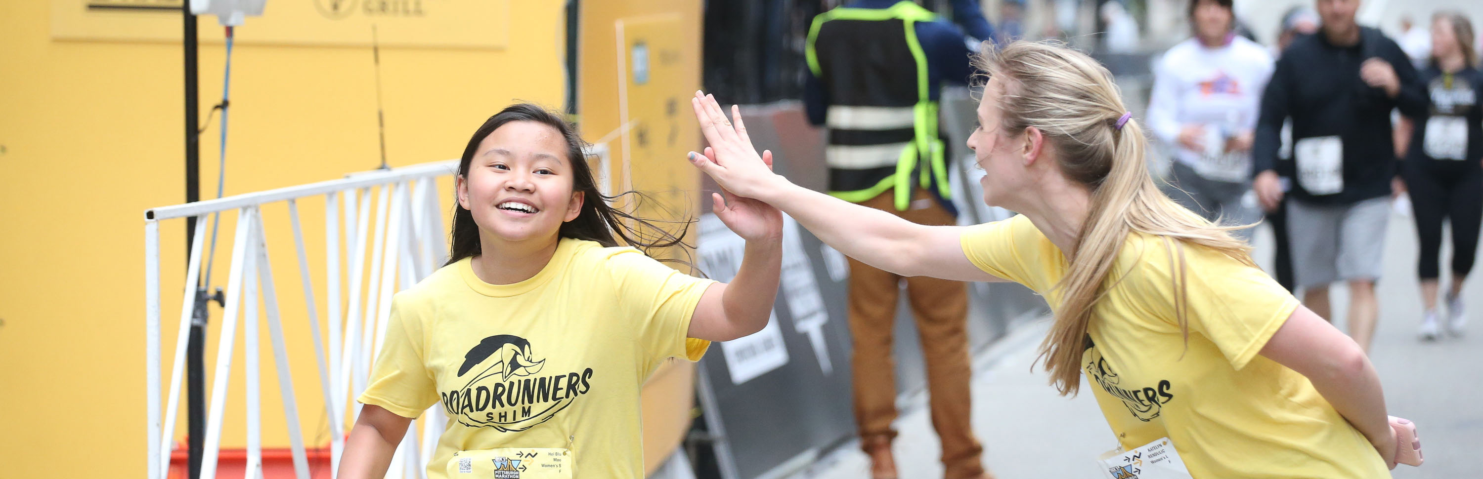 Young girl running in the UPMC Health Plan/UPMC Sports Medicine Pittsburgh 5K gives high-five to young woman