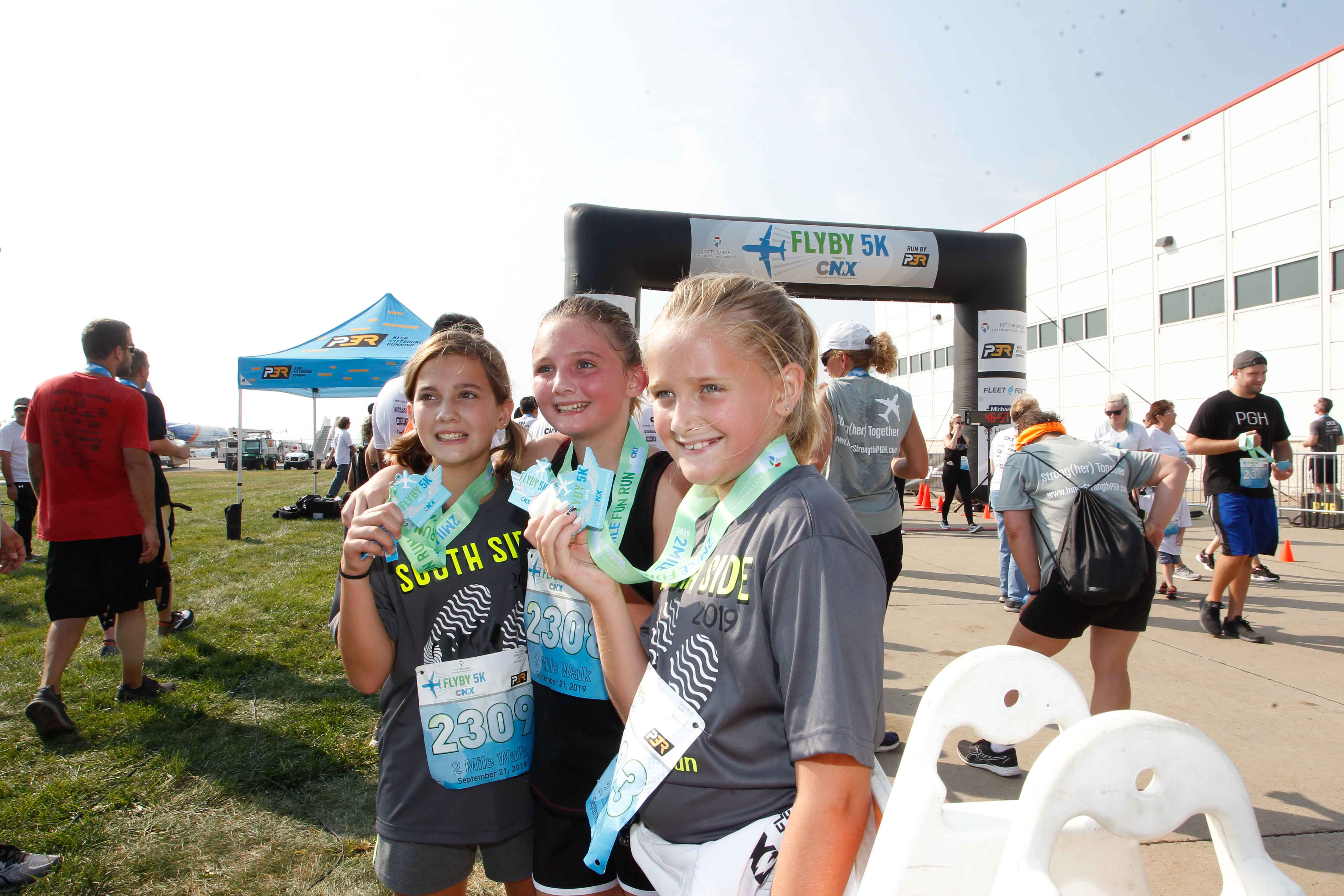 Three young girls showing off their race medals from theFlyBy 5K and 2-Mile Fun Run/Walk presented by CNX Resources