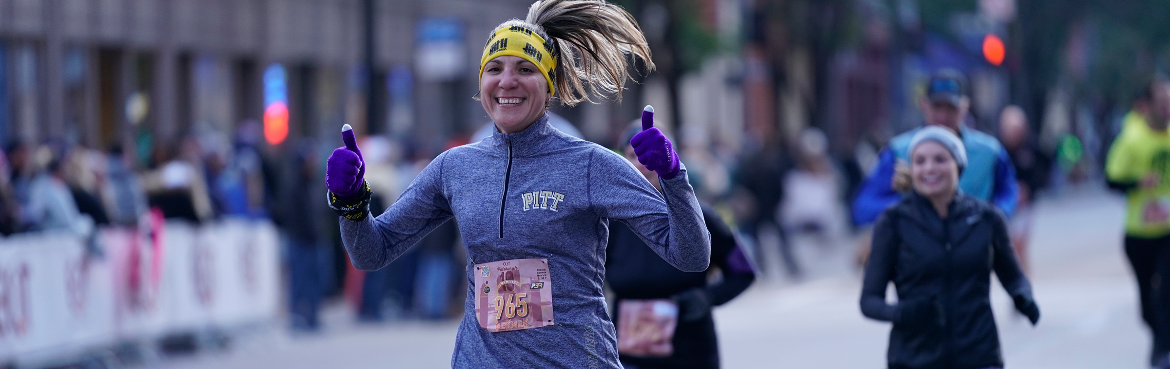 Female runner in a Pitt sweatshirt giving a thumbs-up while running in the DICK'S Sporting Goods Pittsburgh Marathon