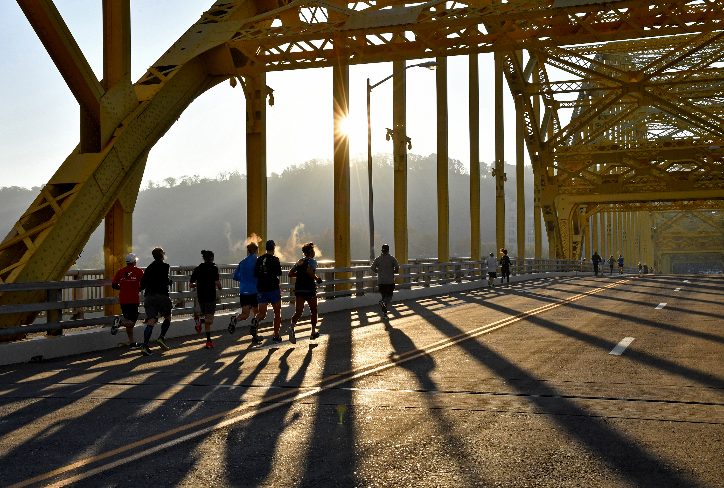 Group of silhouetted runners going over a yellow bridge in the early morning sunlight.