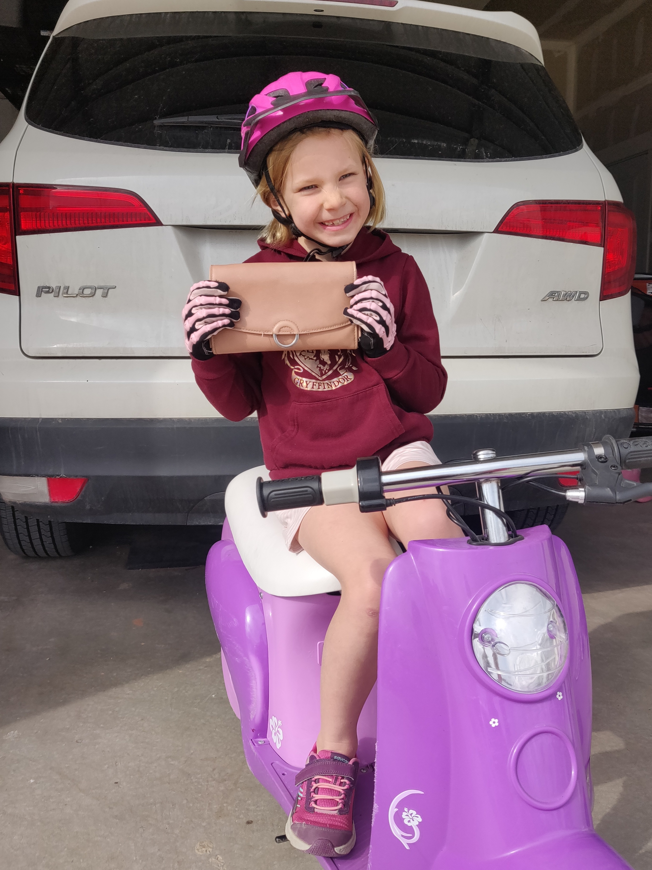 Jared Ward's young daughter holding her wallet while sitting on her new scooter.