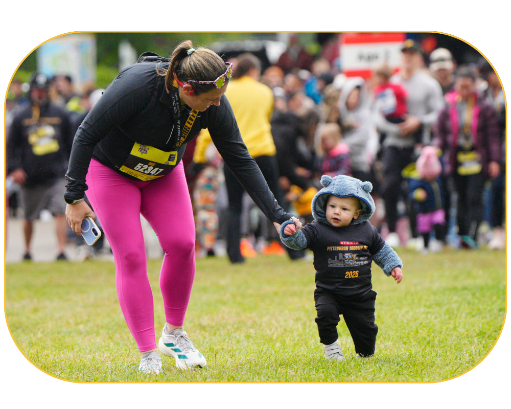 A group of young kids running in the grass at the Sheetz Pittsburgh Toddler Trot with parents behind them